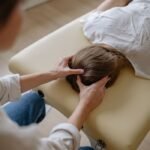 A chiropractor performing a therapeutic head massage on a woman lying on a massage table.
